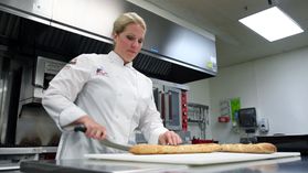 Chef Devin Noor, dressed in her white chef's coat, demonstrates how to breakdown baguettes in one of Tech's test kitchens.